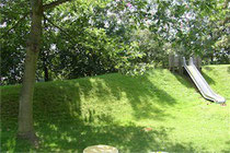 Metallrutsche in einem grasbewachsenen Hügel, neben einem Baum.