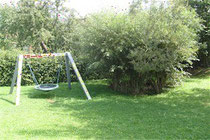 Rundschaukel auf Metallrahmen, umgeben von Gras und Büschen.